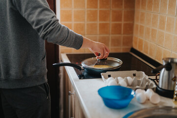 A casual depiction of an individual preparing eggs with a frying pan on a stove top, capturing aspects of food preparation and domestic life.