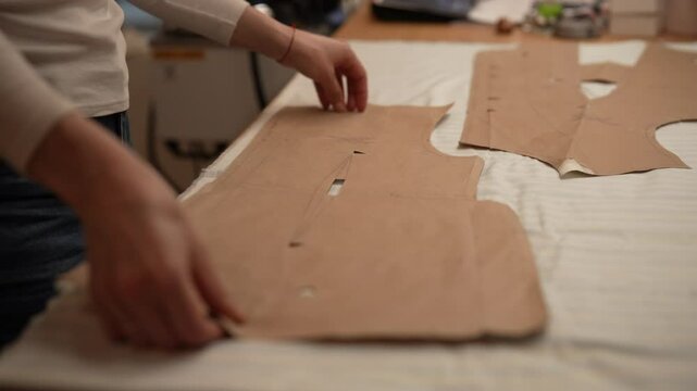 Closeup of seamstress arranging sewing patterns made of cardboard on white striped fabric, preparing to cut material and sew new garment. Concept of sewing manufacturing. Shooting in slow motion.