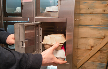 A person holds a carton of eggs in front of a vending machine