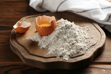 Pile of flour and egg on wooden table, closeup