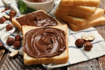 Toasts with chocolate hazelnut spread and nuts on wooden table, closeup