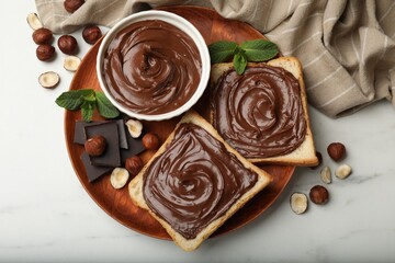 Toasts with chocolate hazelnut spread, nuts, pieces of chocolate and mint on white marble table, flat lay