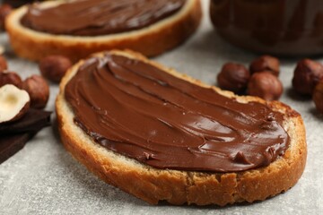 Toasts with tasty chocolate hazelnut spread and nuts on grey table, closeup