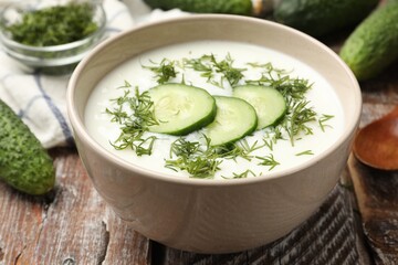 Tasty cucumber soup in bowl and ingredients on wooden table, closeup