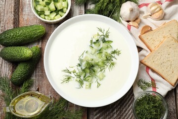 Tasty cucumber soup in bowl and ingredients on wooden table, flat lay