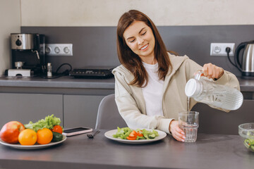 Young Woman Pouring Water into Glass, Enjoying Healthy Meal in Modern Kitchen