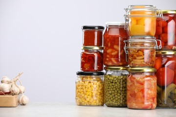 Many jars with different pickled products and ingredients on table against light grey background, space for text