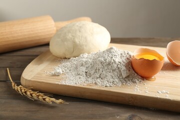 Pile of flour, broken egg and dough on wooden table against grey background, closeup