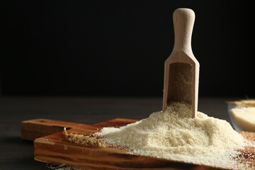 Pile of flour and scoop on dark wooden table against black background, closeup