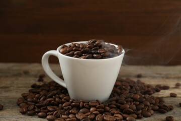 Aromatic coffee beans and cup on wooden table, closeup