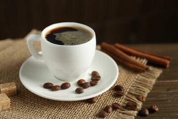 Aromatic coffee in cup, beans, brown sugar and cinnamon on wooden table, closeup