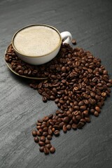 Aromatic coffee in cup and beans on black table, above view