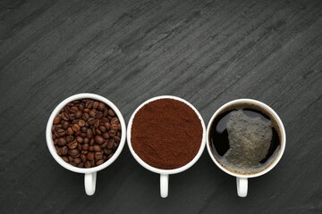 Aromatic ground coffee, beans and hot drink on black table, flat lay. Space for text