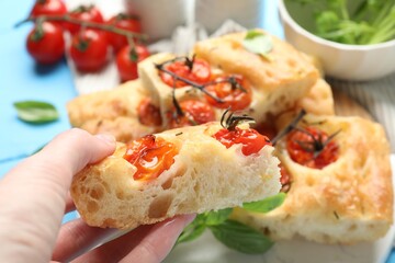 Woman holding piece of delicious focaccia with tomatoes at table, closeup