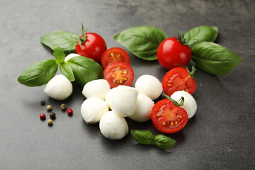 Mozzarella cheese, tomatoes, basil and peppercorns on grey table