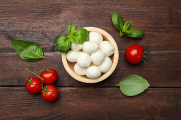 Tasty mozzarella cheese balls, tomatoes and basil on wooden table, flat lay