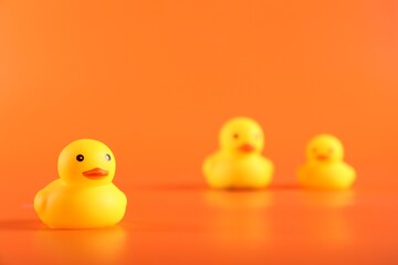 Three cute rubber ducks on orange background, selective focus. Space for text