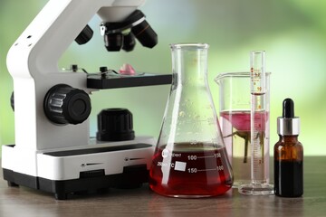 Making luxury perfume. Essential oils in glassware and flowers on wooden table against blurred background, closeup