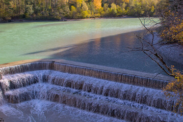 The Lech River in Fussen, Germany, gracefully descends in a series of man-made steps. Sunlight glistens on the water, adding a golden hue to the serene yet powerful scene.
