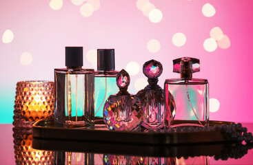 Many different perfume bottles and accessories on mirror surface against pink background with...