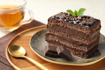 Piece of delicious chocolate cake with mint and tea on table, closeup