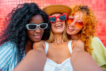 Three happy women taking a selfie with sunglasses and colorful background