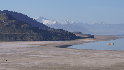 Calm and Serene Lake with Snowcapped Mountains Rising in the Background in Shades of Blue with a Barren Brown Pennisula in the Midground 