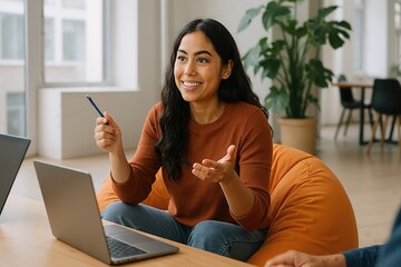 Young woman manager sitting on orange pouf is sharing ideas with colleagues during a business meeting in modern office