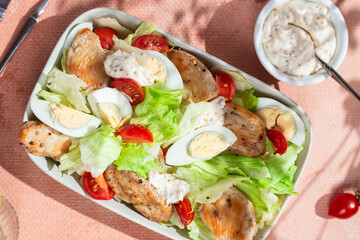 Appetizing salad with chicken, iceberg, eggs, cherry tomatoes in a white plate on the table. Serving breakfast.