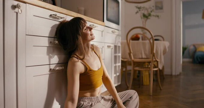 Happy girl in yellow top goes down and squats during her impromptu rest on the kitchen floor in a modern cozy apartment