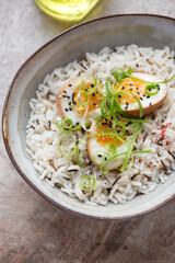 Bowl of mixed rice with soy-marinated chicken eggs and spring onion, vertical shot on a brown granite surface, middle closeup