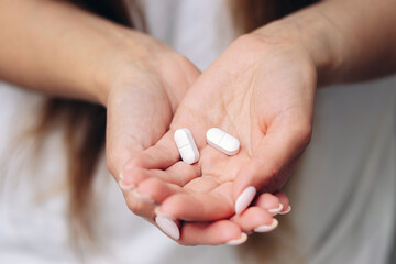 White pills in woman’s hands. Female holding medicine tablets. Close-up of palms with medication. Concept of treatment, health care and pharmacy. Illness cure and pharmaceutical product.