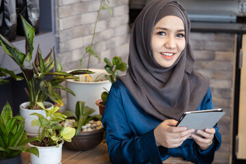 Asian female Muslim Digital Nomad Worker working remotely in cafe, happy smiling positive mood and facial expression