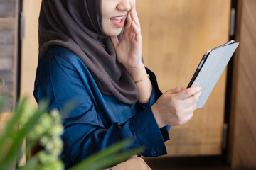 Successful Asian female Muslim Digital Nomad Worker working remotely in cafe, happy smiling exciting mood and facial expression, closeup shot