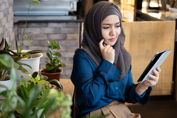 Asian female Muslim Digital Nomad Worker working remotely in cafe, thinking, planning when having work problem