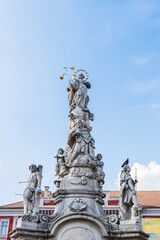 Detailed view of a tall, ornate stone monument adorned with multiple figures and sculptures, standing prominently in Timisoara's historic Liberty Square, Romania.