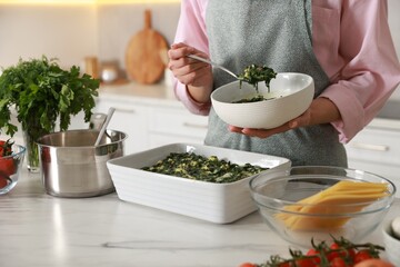 Woman making spinach lasagna at marble table indoors, closeup