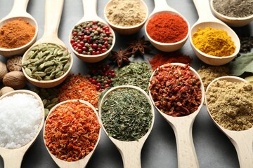 Many different spices in spoons on grey table, closeup