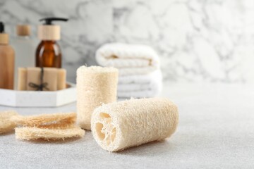 Different loofah sponges and cosmetic products on light grey table, closeup. Space for text
