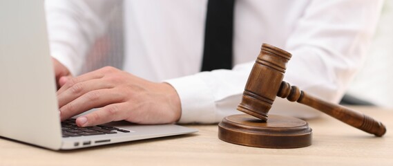 Judge working with laptop and gavel at desk indoors, closeup