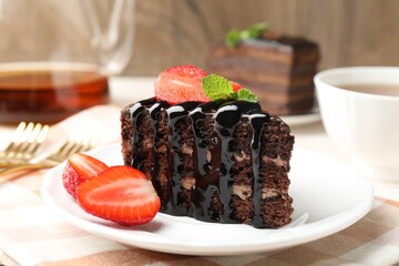 Piece of chocolate cake served with strawberries and tea on table, closeup