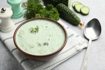 Tasty cucumber soup, spoon and ingredients on light grey table, closeup