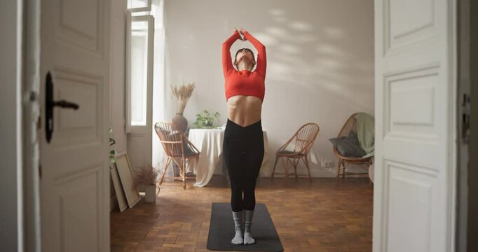 Girl in sportswear starts her yoga and meditation and gets into warrior pose on gym mat at home. Beginning of yoga and gassho position at home