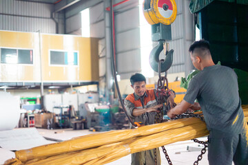 Obraz premium Workers collaborating to lift equipment with a crane in an industrial warehouse during daytime