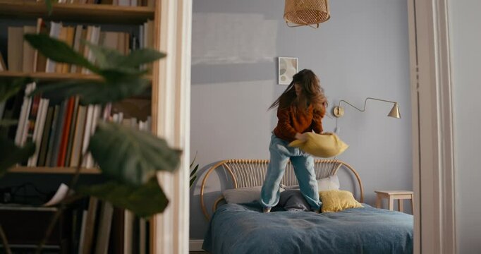 Girl in casual clothes dancing on bed cheerful active energetic dance holds pillow in hands during her self-expression at home in modern cozy apartment