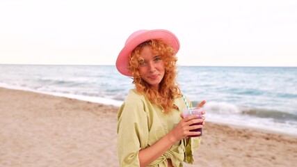 Young redheaded woman in pink hat enjoying refreshing juice while relaxing on sunny tropical beach, sipping through straw with serene ocean backdrop - Powered by Adobe