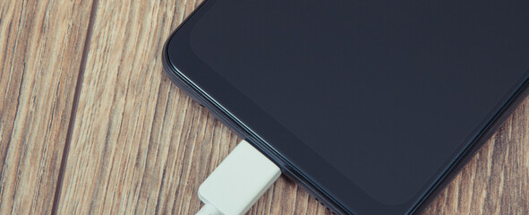 Black smartphone and connected cable of charger. Telephone charging
