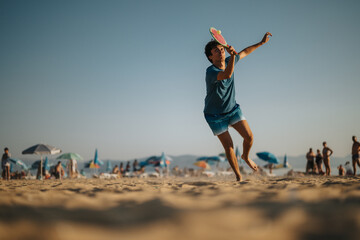A young man energetically plays beach ball on the sandy shore under a sunny sky. Umbrellas and...
