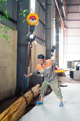 Worker manages heavy load using a crane in a factory setting during daylight hours