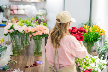 Florist arranging red roses amidst a vibrant display of fresh flowers in a bright and tidy shop...